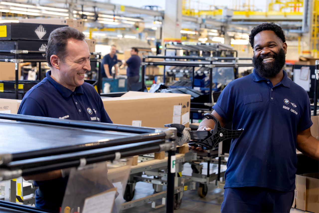 Zwei Männer in blauen Shirts stehen in einer Fabrik und diskutieren über die Produktionslinie.