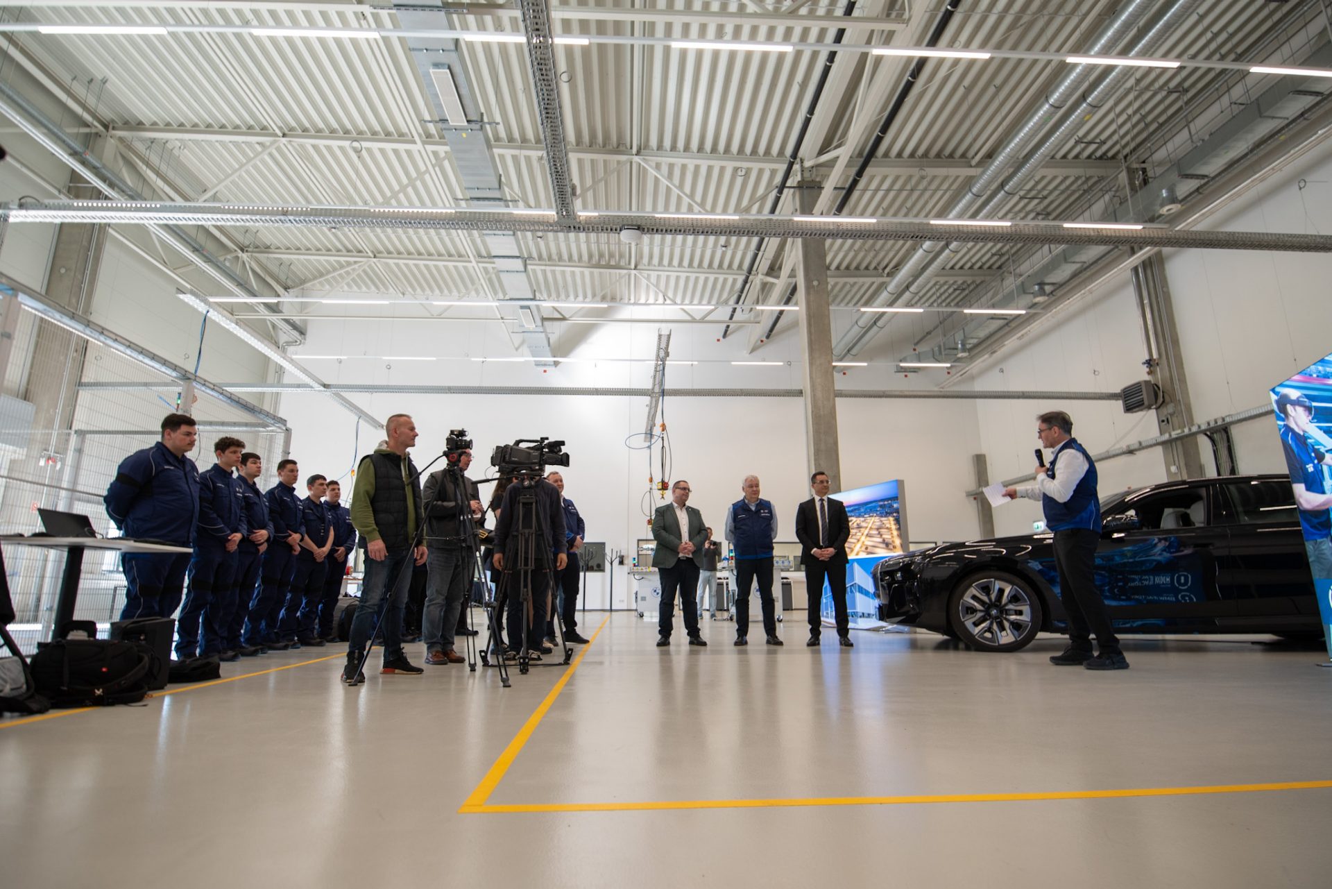 People are standing in a hall and someone is giving an interview in front of a camera