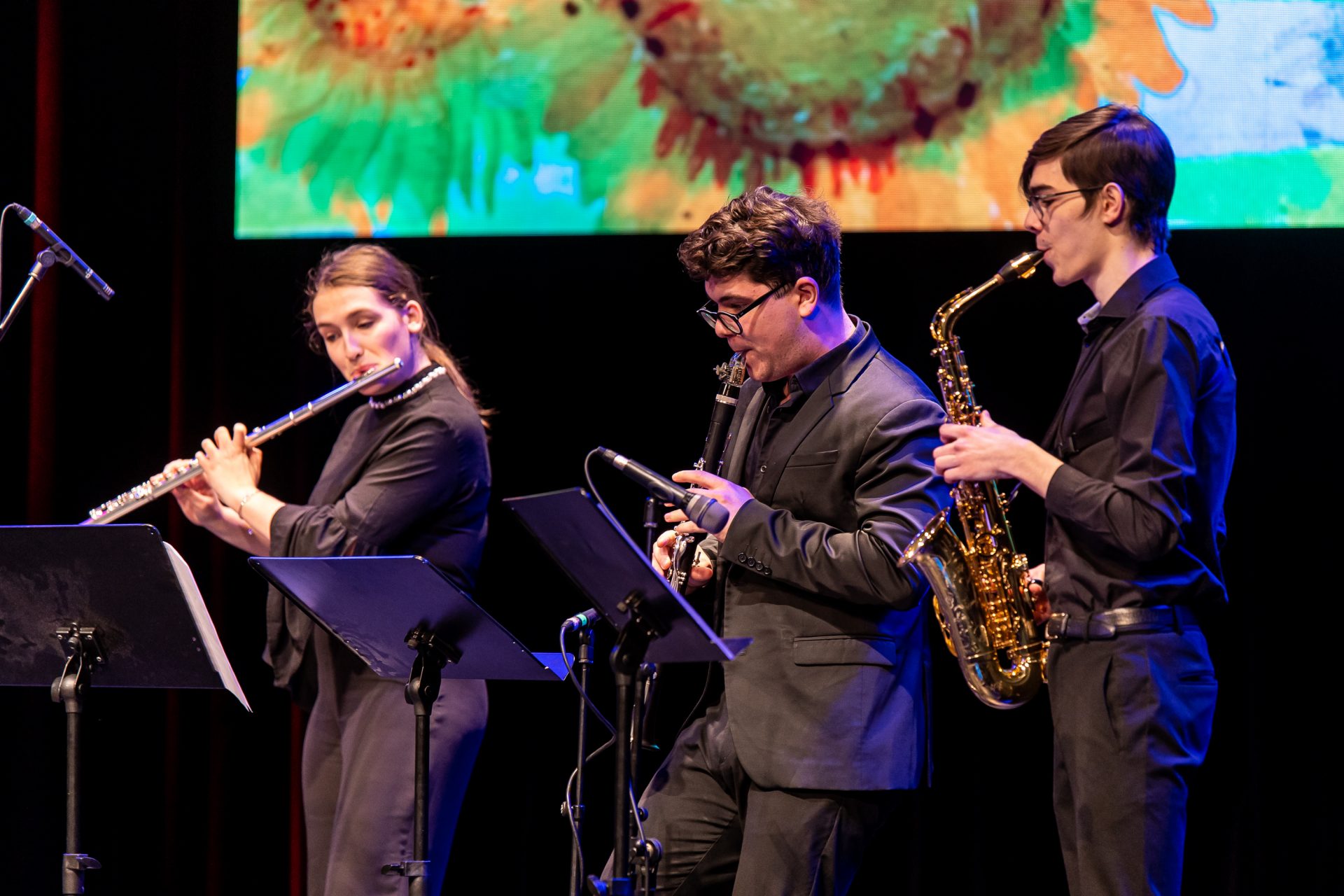 Three people standing on the stage playing an instrument.