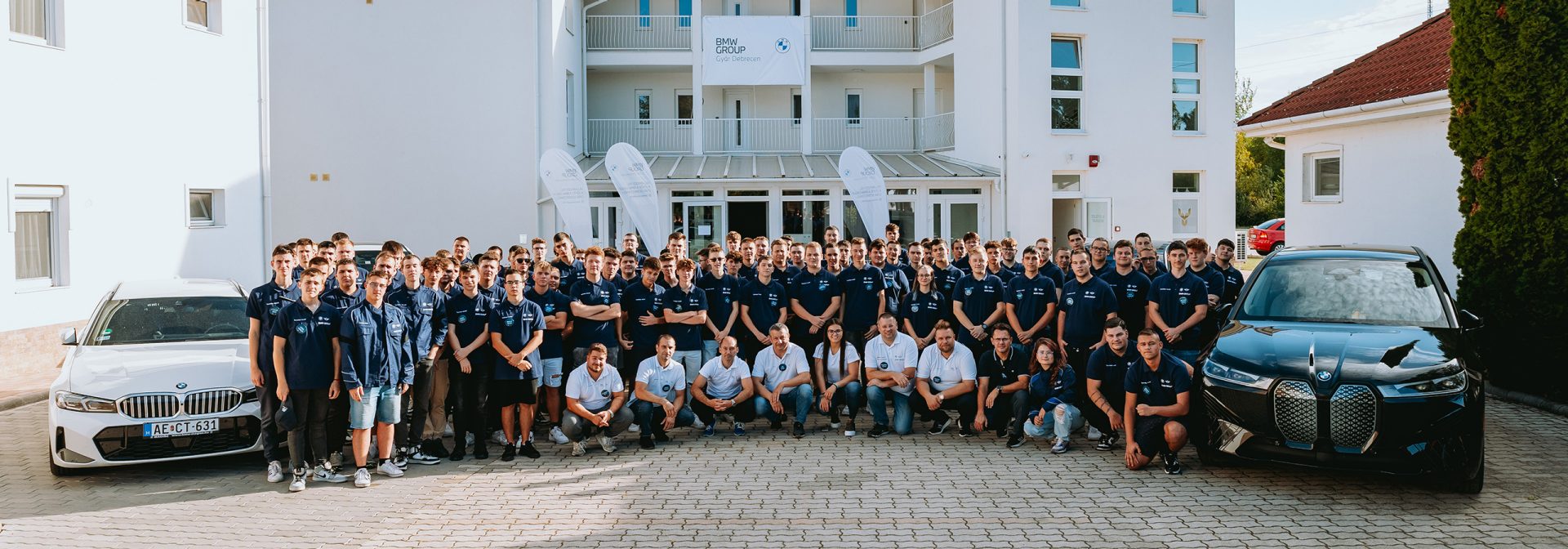 apprentices standing next to two BMW cars