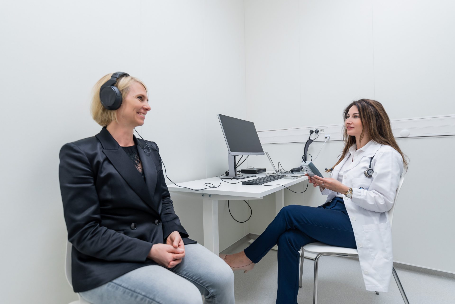 A woman with headphones is sitting in front of an employee who has a device to control the headphones