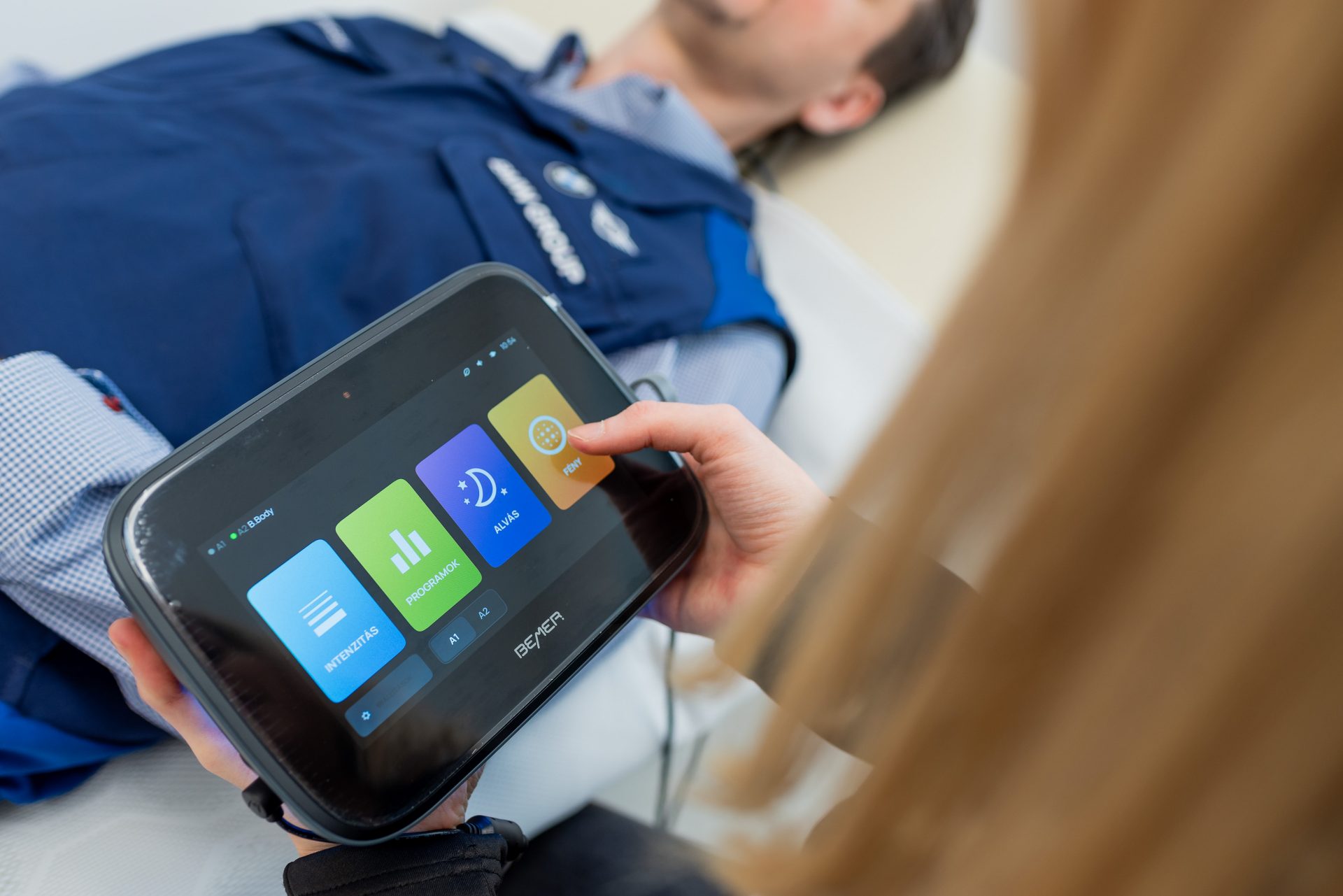 A man is laying in a bed and a woman is adjusting something on a tablet