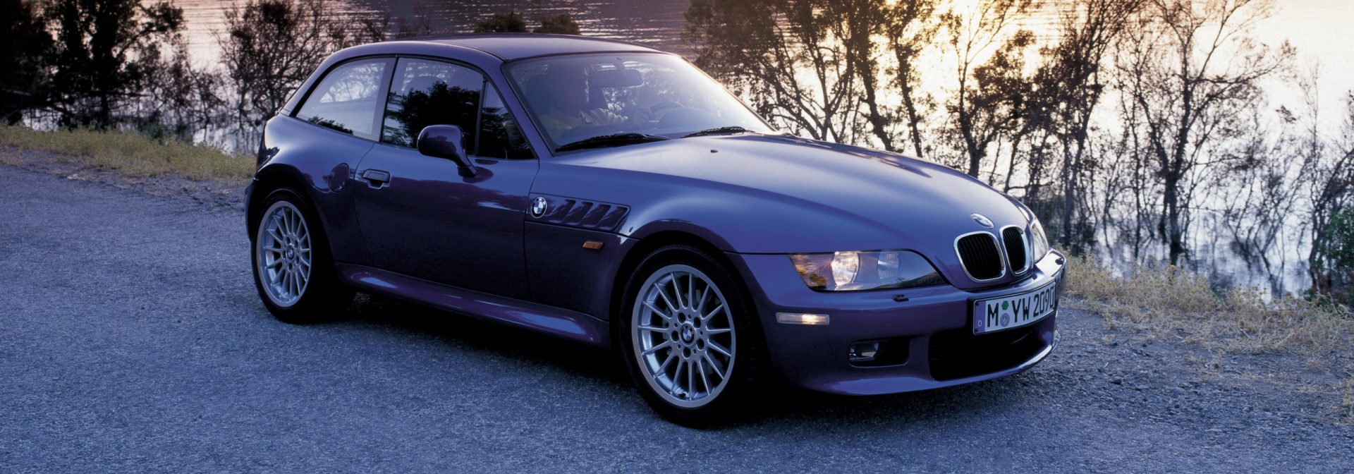 BMW Z3 Coupe and M Coupe begin assembly at Plant Spartanburg. Vehicle parked on gravel road with trees in background. 