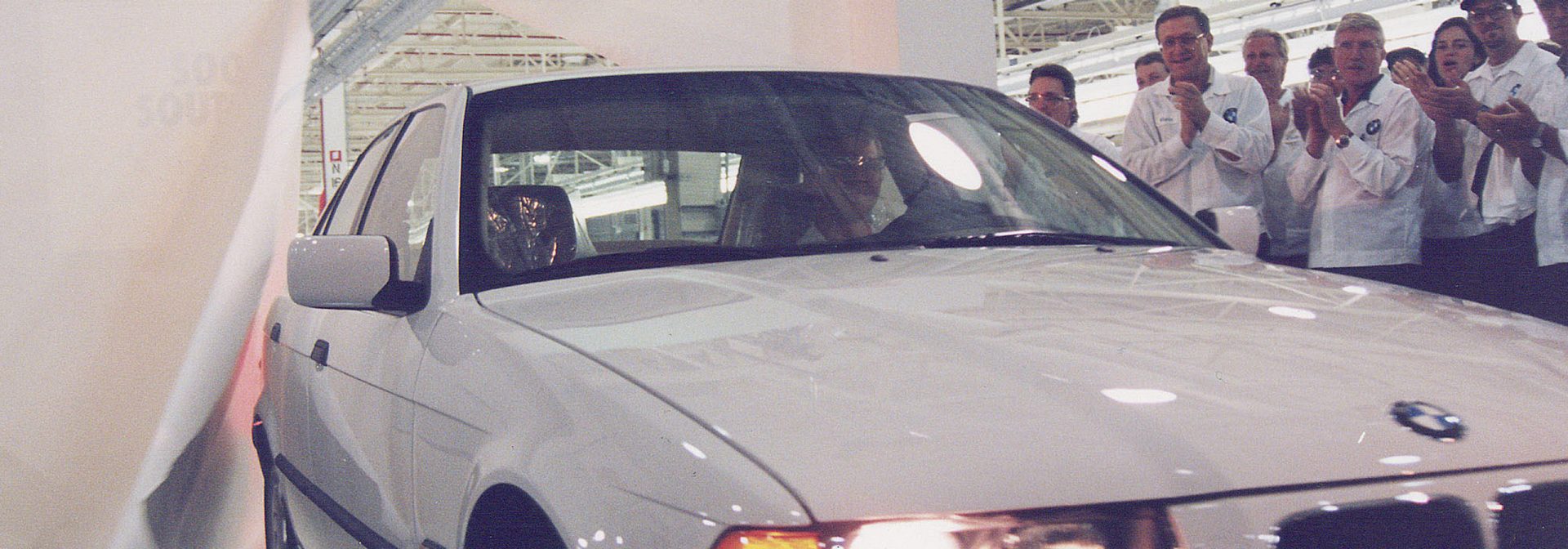 First BMW rolls off the line as associates gather around and celebrate by clapping. 