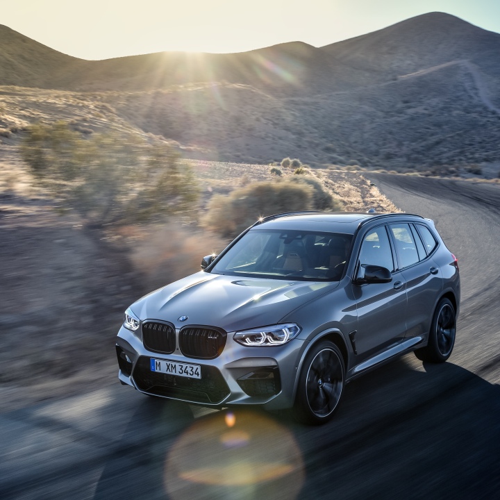 BMW X Model driving around corner on a desert road. 