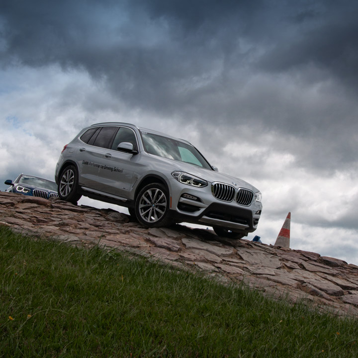 BMW Performance Center Driving School participant navigates a BMW X5  as it descends down a rocky hill. 