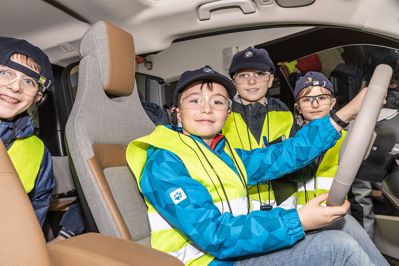 4 Kinder mit Warnwesten und Schutzbrillen in einem BMW i3