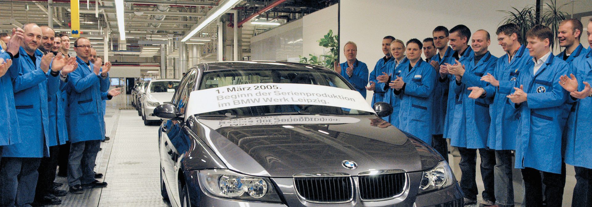 Several men gather around a 2005 BMW 3 Series and clap.