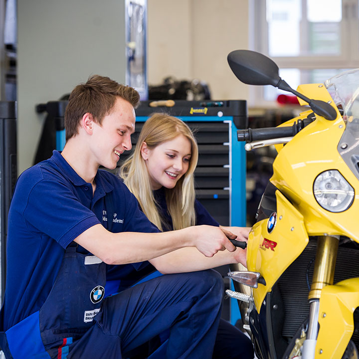 Two student interns working on a yellow BMW motorcycle.