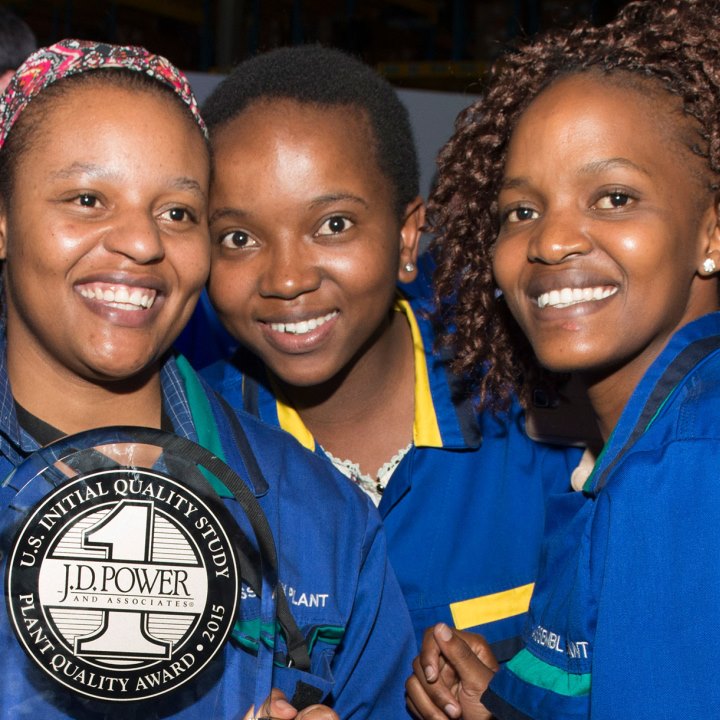 A group of three women in matching blue attire holds a plaque, showcasing their achievement with smiles.
