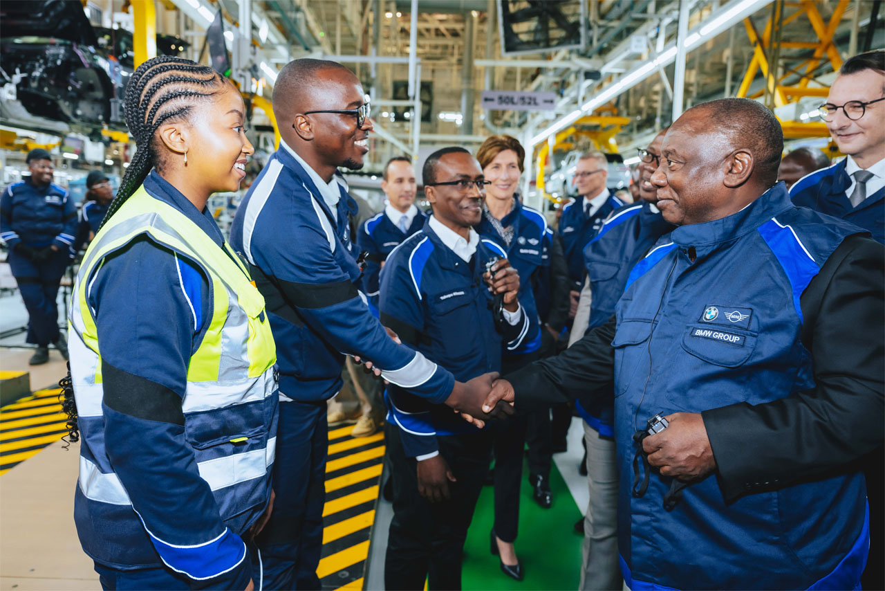 A team dressed in blue jackets and shirts gathers in front of a vehicle.